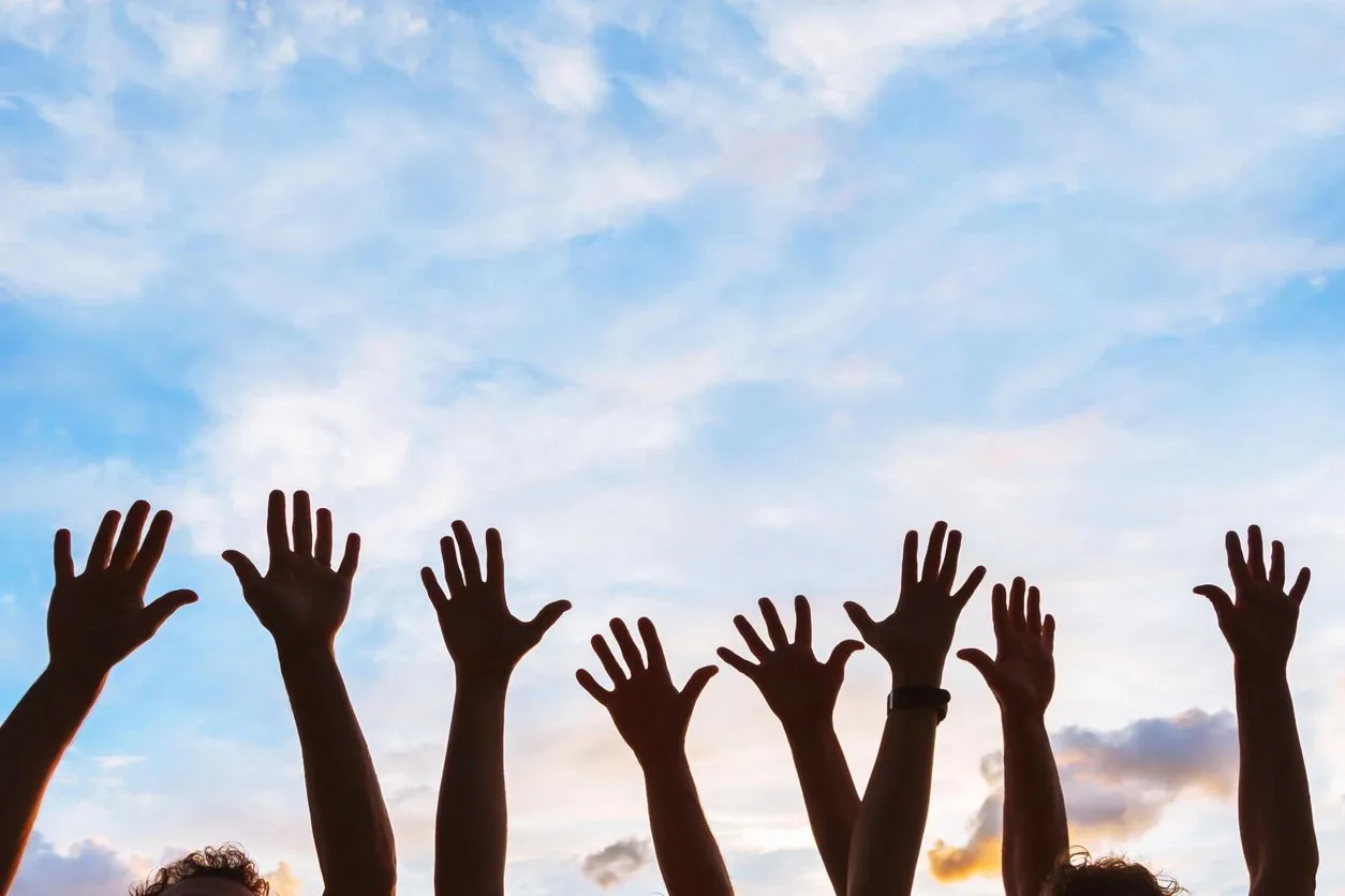 Many hands raised together against a blue sky.